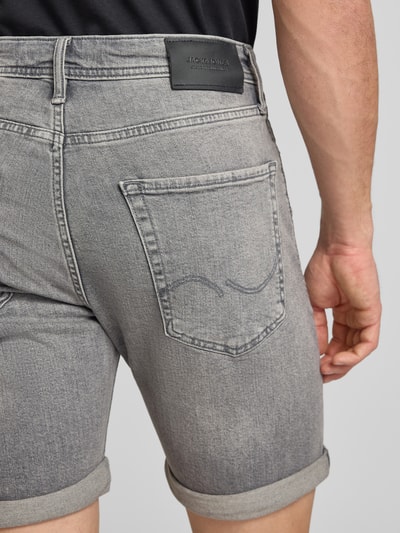 Männermodel trägt Regular Fit Jeansshorts mit Umschlag Modell 'RICK' von Jack & Jones aus grauem Baumwoll-Elasthan-Mix, Nahaufnahme Rückansicht. Herren Jeansshorts mit Eingrifftaschen, Bundweite bei Größe M 42 cm, Innenbeinlänge 21 cm.