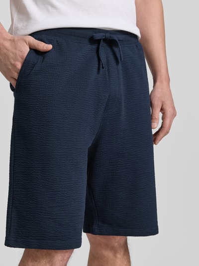 Mężczyznę nosi Relaxed Fit Bermudas aus Baumwoll-Mix Modell 'DETROIT' od s.Oliver RED LABEL, granatowy kolor, faktura waflowa, elastyczny pas z troczkiem, bawełna-mix, kieszenie po bokach i z tyłu, uniseks, zbliżenie na górną część ciała.