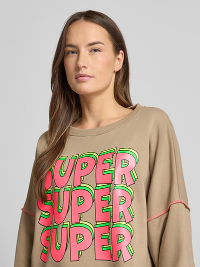 Frauenmodel trägt Oversized Sweatshirt mit gerippten Abschlüssen von miss goodlife, Statement-Print, Beige mit Neonfarben, Nahaufnahme Oberkörper.