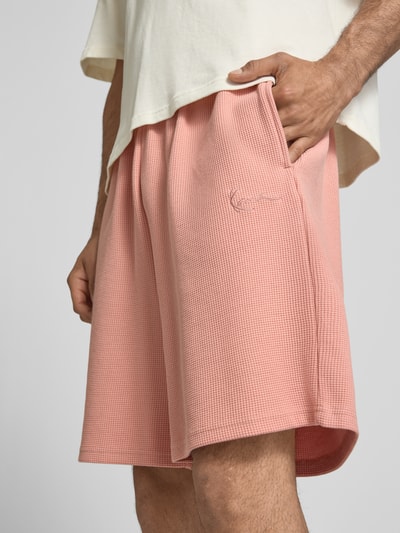 Männermodel trägt Regular Fit Shorts mit Strukturmuster von KARL KANI in Rosa, Baumwoll-Mix, Logo-Stitching, Nahaufnahme Oberschenkel.