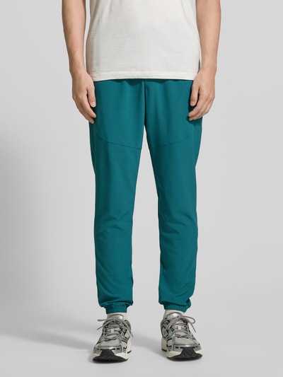 Männermodel trägt Regular Fit Jogger mit Logo-Print Modell 'Vibe' von Under Armour in Türkis, elastischer Bund, Eingrifftaschen, Ganzkörperansicht von vorne.
