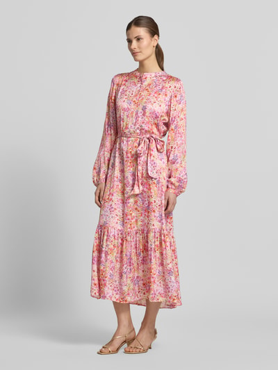 Frauenmodel trägt Midikleid aus Viskose mit Bindegürtel von Rich & Royal, florales Allover-Muster in Rosa, A-Linie, Ganzkörperansicht von vorne.