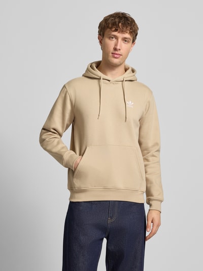 Mężczyznamodel nosi Hoodie mit Känguru-Tasche od adidas Originals z mieszanki bawełny, krój regular fit, wyhaftowane logo, kieszeń kangurka, jasnobeżowy kolor, gładka tekstura, przód całego ciała.