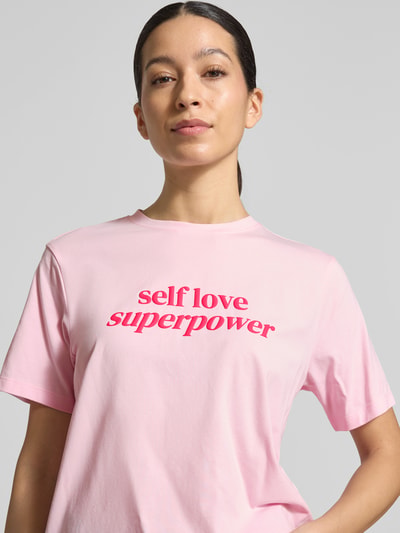 Frauenmodel trägt T-Shirt mit geripptem Rundhalsausschnitt Modell 'NORA' von Vila, rosa Baumwoll-Elasthan-Mix, lockerer Schnitt, Nahaufnahme Oberkörper.