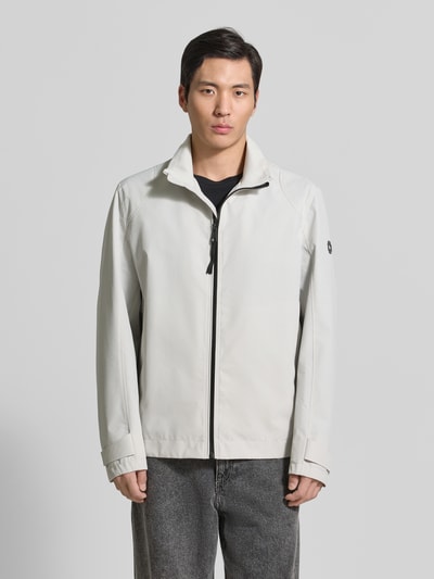 Męski model nosi Regular Fit Funktionsjacke aus wasserdichtem Material Modell 'LUCCA' od Strellson, jednolita szarość, metalowa aplikacja logo, długi rękaw, stehkraag, zapięcie na zamek, kieszenie boczne na zamek, funkcje: wiatroszczelna, wodoodporna; zdjęcie całej sylwetki z przodu.