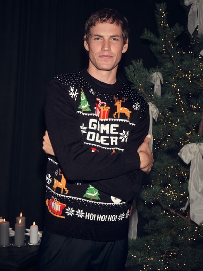 Męski model nosi Strickpullover mit gerippten Abschlüssen von Montego, czarny, wzór świąteczny, regular fit, okrągły dekolt, widok z przodu, ujęcie całej sylwetki.