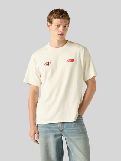 Männermodel trägt Relaxed Fit T-Shirt aus reiner Baumwolle von Levi's®, helles Creme mit roten Details, glatte Textur, Ganzkörperansicht von vorne.