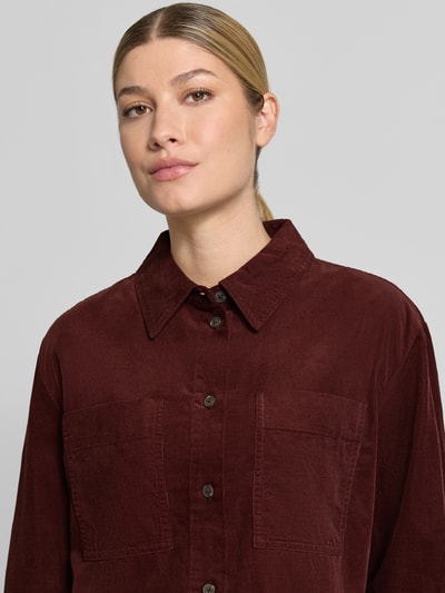 Frauenmodel trägt Regular Fit Langarmbluse aus reiner Baumwolle Modell 'Fronna' von OPUS in dunklem Rotbraun, sichtbare Knopfleiste und Brusttaschen, glatte und strukturierte Cord-Optik, Damen Langarmbluse, Nahaufnahme Oberkörper.