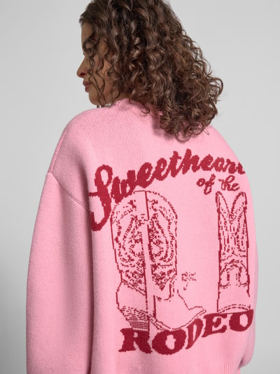 Frauenmodel trägt Relaxed Fit Pullover in Strick-Optik von ANOTHER COTTON LAB, rosa mit rotem Logo-Stitching, Nahaufnahme Rückansicht.
