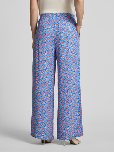 Frauenmodel trägt Wide Fit Stoffhose aus reiner Viskose mit Allover Motiv-Print von Smith and Soul, blaue Grundfarbe, elastischer Bund, Ganzkörperansicht Rückansicht.