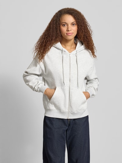 Kobiece modelka ma na sobie Oversized Fit Sweatjacke mit geteilter Kängurutasche od Gina Tricot, mieszanka bawełny, krój oversized fit, kieszeń kangurka, kaptur z tunelem, elastyczne wykończenia, jasnoszary, faktura dzianiny, przód bluzy, zdjęcie całej sylwetki z przodu.
