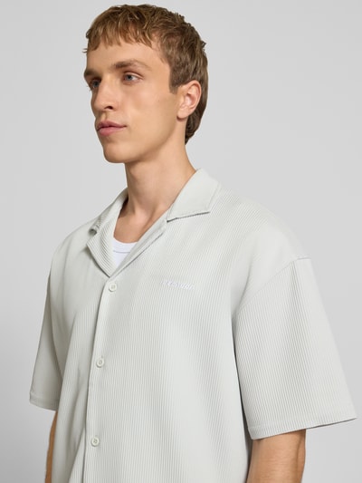 Männermodel trägt Relaxed Fit Freizeithemd mit Reverskragen Modell 'Troy' von Pegador, hellgraue Farbe, Strukturmuster, Logo-Stitching, kurzärmelig, durchgehende Knopfleiste, Ganzkörperansicht von vorne