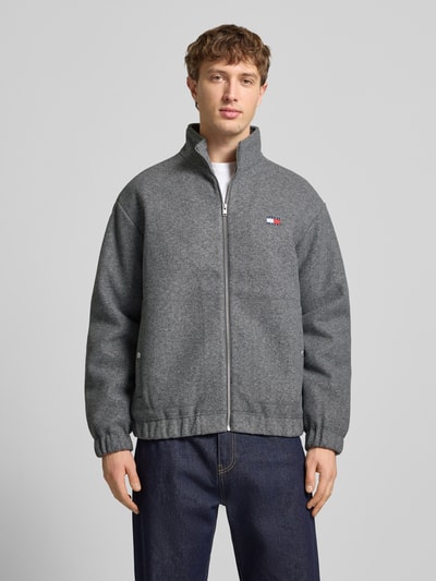 Mężczyzna prezentuje Regular Fit Bomberka z dodatkiem wełny od Tommy Jeans, melanż, stójka, zamek błyskawiczny, logo, wpuszczane kieszenie, długi rękaw, elastyczne zakończenia, całkowity widok z przodu.