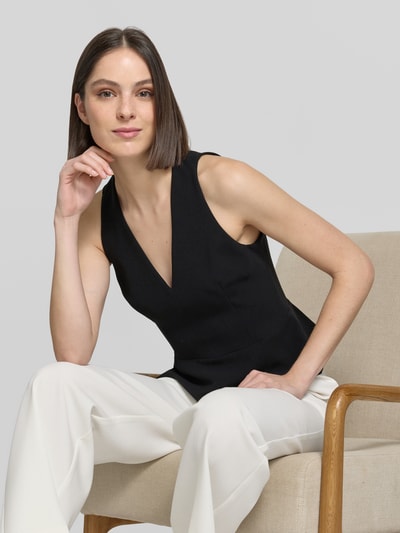 Frauenmodel trägt Slim Fit Blusentop mit Schößchen von HUGO in Optik: Unifarben, Passform: Slim-Fit, V-Ausschnitt, Reißverschluss, Ärmelform: ohne Arm, Rumpfabschluss: ausgestellt, schwarze glatte Struktur, Ganzkörperansicht von vorne.