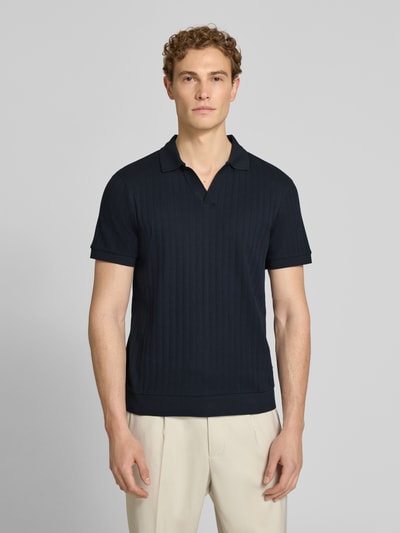 Męski model nosi koszulkę polo Regular Fit Poloshirt mit V-Ausschnitt Modell 'Baronito' von JOOP! Collection z bawełny o fakturowanym wzorze, dekolt w serek, długość tyłu w rozmiarze M: 69 cm, kolor granatowy; całkowity widok z przodu