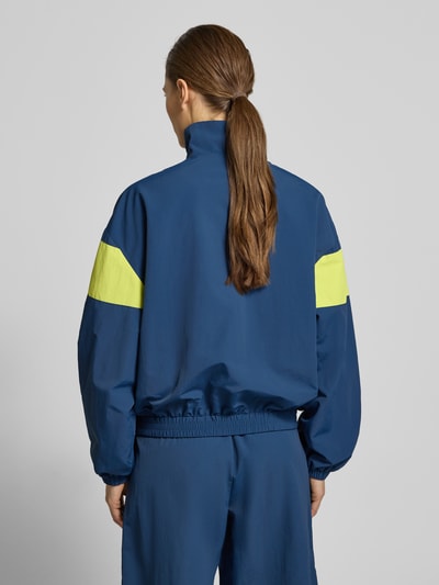 Vrouwenmodel draagt Nylon-Jacke im 90s-Stil - curated by Tinvcb van Tinvcb in blauw met gele accenten, regular fit, elastische boorden, steekzakken met rits, staande kraag, ruglengte 60 cm, schouderbreedte 54 cm, borstwijdte 58 cm, mouwlengte 34 cm, volledig van achteren gezien.