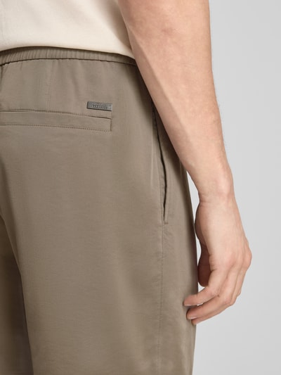 Männermodel trägt Regular Fit Stoffhose aus Viskose-Mix mit elastischem Bund von ARMANI EXCHANGE, Detailaufnahme Rückansicht, Ziernähte, Gesäßtaschen, glatte beige Oberfläche, Kontext: Herren Stoffhose, Bundweite 44 cm, Innenbeinlänge 77 cm.