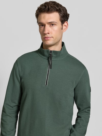 Männermodel trägt Relaxed Fit Sweatshirt aus Baumwoll-Mix Modell 'SELANIK' von LERROS in dunklem Grün mit Troyer-Kragen, Nahaufnahme Oberkörper.