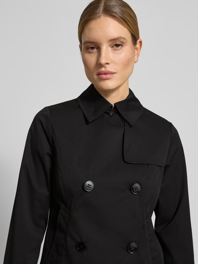 Modelka kobieca nosi Trenchcoat mit Knopfverschluss od MICHAEL Michael Kors, czarny, krój regular fit, z kołnierzem i dwurzędowym zapięciem, szerokość w rozmiarze S: 52 cm, długość pleców: 61 cm, szerokość ramion: 40 cm, długość rękawa: 63 cm, tekstura gładka, zbliżenie na górną część ciała, z przodu.