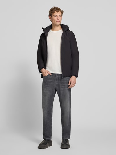 Męski model nosi Regular Fit Jacke mit Logo-Print von Lindbergh, czarny kolor, elastyczna mieszanka materiałów, kaptur z tunelem, nadruk z logo, kieszeń napoleonka, długość tyłu w rozmiarze M: 74 cm, szerokość ramion w rozmiarze M: 46 cm, szerokość klatki piersiowej w rozmiarze M: 42 cm, długość rękawów w rozmiarze M: 62 cm, pełen widok z przodu