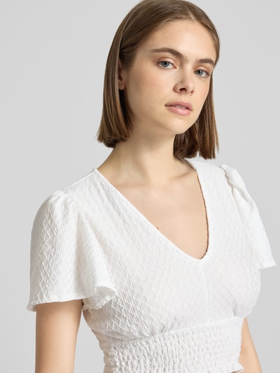 Vrouwenmodel draagt Regular Fit Crop Top met structuurpatroon model 'HANNAH' van Only in effen wit, gesmokte borstband, V-hals, vlindermouwen, korte mouw, smok bij de zoom. Detailopname bovenlichaam.