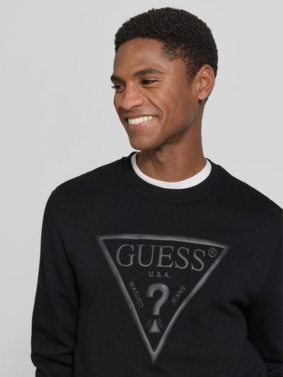 Männermodel trägt Regular Fit Sweatshirt mit Logo-Detail Modell 'Audley' von Guess, Baumwoll-Mix, schwarze Farbe, Nahaufnahme Oberkörper.