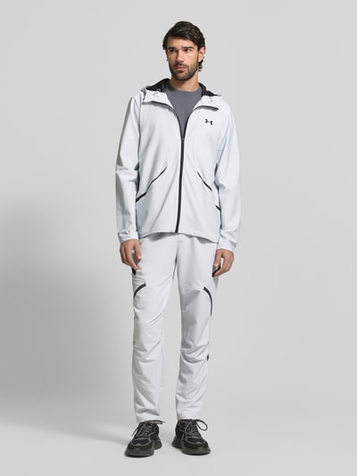 Männermodel trägt Regular Fit Sweatpants mit Logo-Print Modell 'Unstoppable' von Under Armour im Elastischer-Material-Mix, Cargo-Taschen mit Reißverschluss, Elastischer Bund, Farbe Hellgrau, Herren, Regular-Fit, Ganzkörperansicht von vorne.