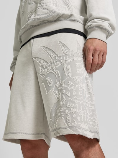 Männermodel trägt Straight Fit Shorts mit Baumwoll-Anteil von Diesel in hellem Beige, mit Strukturmuster, elastischem Bund, Gesäßtasche, Nahaufnahme Oberschenkel, Material-Mix, Logo-Detail sichtbar, Innenbeinlänge 23 cm bei Größe M, Bundweite 41 cm bei Größe M.