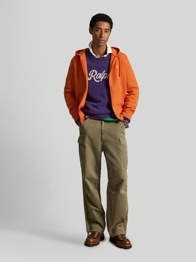 Męski model nosi Regular Fit Sweatjacke aus Baumwoll-Mix von Polo Ralph Lauren w kolorze pomarańczowym, tekstura gładka, Ganzkörperansicht von vorne.