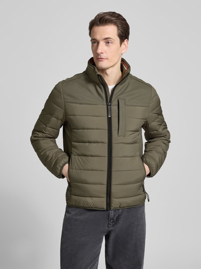 Męski model nosi Regular Fit Steppjacke mit seitlichen Stretcheinsätzen von Tom Tailor, jednokolorowy, stójka, krój regular fit, zamek błyskawiczny, naszywka z logo, pas na plecach, boczne panele stretch, długie rękawy, elastyczne wykończenia, hydrofobowy, kieszeń wewnętrzna, boczne kieszenie na zamek, brustasza, widok całej sylwetki z przodu.