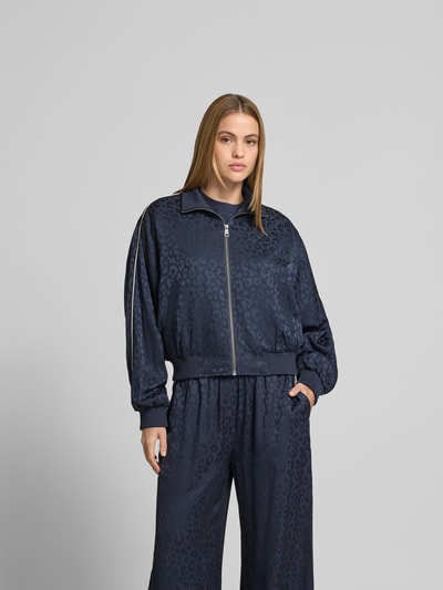 Frauenmodel trägt Tracksuit-Jacke aus Viskose-Mix von Lala Berlin, dunkelblau mit Allover-Animal-Print, Reißverschluss, Ganzkörperansicht von vorne.