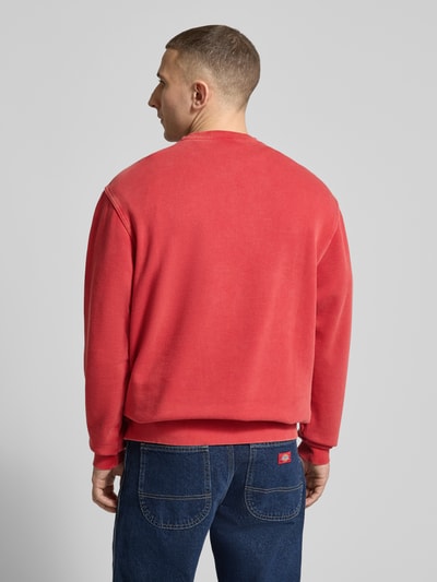 Mannenmodel draagt Sweatshirt mit Label-Stitching und Rundhalsausschnitt van Dickies in rood, katoenmix, relaxed fit, ruglengte maat M 69 cm, mouwlengte maat M 68 cm, ganzkörperaanzicht rugaanzicht.