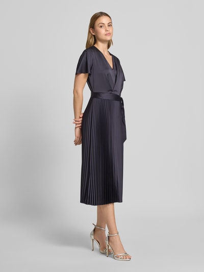Frauenmodel trägt Midikleid aus Satin mit V-Ausschnitt von Comma, taillierte Passform, Plissee-Optik, abnehmbares Stoffband, dunkelblau, glänzende Textur, Ganzkörperansicht von vorne.