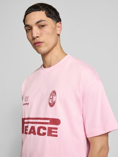 Männermodel trägt Oversized T-Shirt mit Logo-Print von ANOTHER COTTON LAB in Rosa, reine Baumwolle, Rundhalsausschnitt, Nahaufnahme Oberkörper.