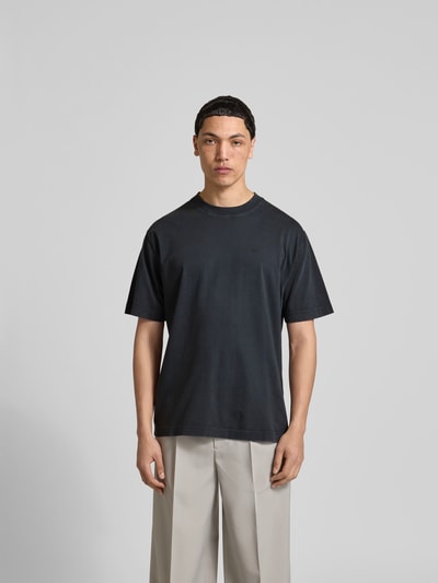 Männermodel trägt Regular Fit T-Shirt aus reiner Baumwolle von Closed in Schwarz, Rundhalsausschnitt, Used-Look, Label-Print, Ganzkörperansicht von vorne. Rückenlänge bei Größe M: 76 cm.