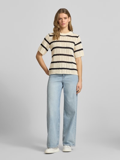 Frauenmodel trägt Regular Fit Strickshirt aus reiner Baumwolle Modell 'NUKA' von Pieces mit Optik:Allover-Muster, gestreift, Lochstrick, in Creme und Schwarz, Rundhals-Ausschnitt, Kurzarm, ganzkörperansicht von vorne.