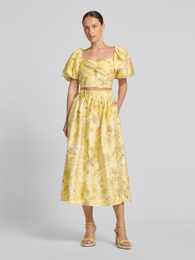 Frauenmodel trägt Cropped Blusentop mit Puffärmeln Modell 'LEMON' von YAS aus Lyocell-Mix mit Leinen-Anteil, gelber Allover-Look, Knotendetail, Ganzkörperansicht von vorne.