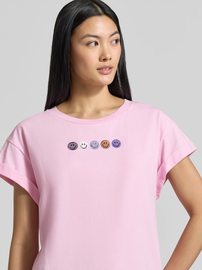 Frauenmodel trägt Relaxed Fit T-Shirt aus reiner Baumwolle von Rich & Royal, rosa, fixierte Ärmelumschläge, Ziersteine, Nahaufnahme Oberkörper.