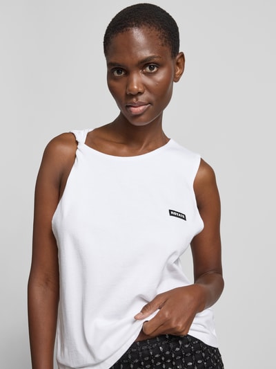 Frauenmodel trägt Relaxed Fit Top mit Logo-Patch von ROTATE in Weiß aus reiner Baumwolle mit Rundhalsausschnitt und Twist-Detail, Nahaufnahme Oberkörper.
