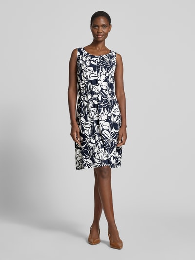 Frauenmodel trägt Knielanges Kleid aus Viskose-Mix mit Rundhalsausschnitt von Betty Barclay, florales Muster in Dunkelblau und Weiß, Taillierter Schnitt, Stretch-Anteil, Knielänge, Rückseitiger Schlüsselloch-Ausschnitt mit Bindung, Rückenlänge 97 cm, Brustweite 39 cm bei Größe 36, Ganzkörperansicht von vorne.