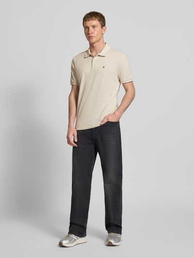 Männermodel trägt Straight Fit Poloshirt mit Label-Stitching von Calvin Klein Jeans aus reiner Baumwolle, Polokragen, gerippte Ärmelabschlüsse, Ganzkörperansicht von vorne.