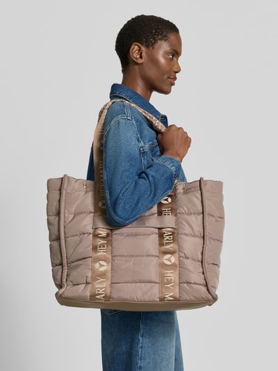 Frauenmodel trägt Shopper mit Label-Details Modell 'Best Buddy' von Hey Marly in Beige mit Hauptfach, Reißverschluss, Lange Trägergriffe, Ganzkörperansicht von der Seite. Breite 42 cm, Länge 36 cm, Tiefe 16 cm, Schulterriemen 63 cm, strukturierte Oberfläche.