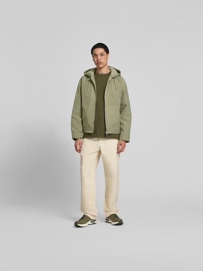 Männermodel trägt Regular Fit Jacke mit Kapuze von WON HUNDRED in Grün, geteilter Känguru-Tasche, Reißverschluss, Ganzkörperansicht von vorne.