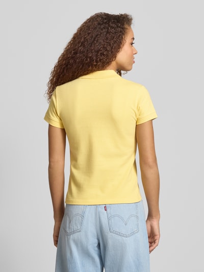 Frauenmodel trägt kurzärmliges Poloshirt in Piquéoptik mit Kragen und Logostickerei von REVIEW aus reiner Baumwolle, Slim Fit, gelb, Rückenlänge bei Größe S 52 cm, Ganzkörperansicht Rückansicht.