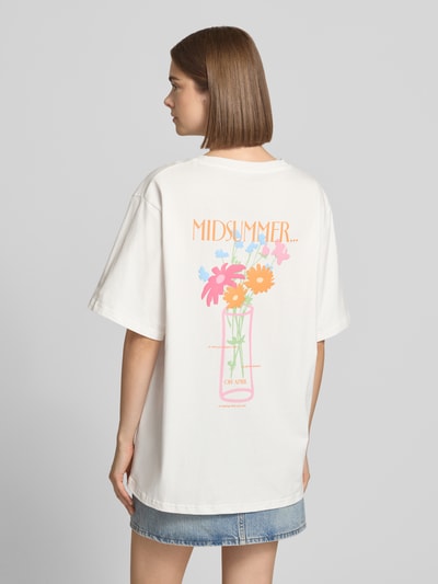 Frauenmodel trägt Oversized T-Shirt mit Rundhalsausschnitt Modell 'Midsummer' von OH APRIL in Weiß mit buntem Print, Ganzkörperansicht Rückansicht. Reine Baumwolle, Rückenlänge Größe S 70 cm.