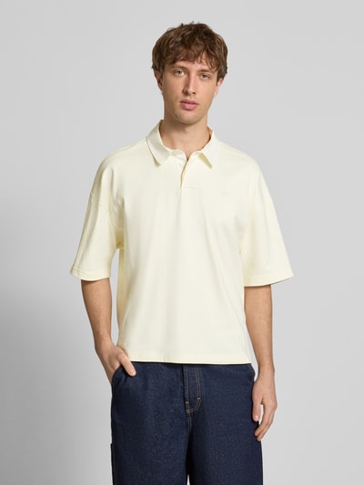 Männermodel trägt Regular Fit T-Shirt mit Polo-Kragen von adidas Originals in Creme, reine Baumwolle, Logo-Stitching, Ganzkörperansicht von vorne.
