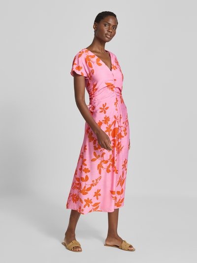 Frauenmodel trägt Midikleid aus Viskose-Mix Modell 'Jamie' von MANGO mit floraler Musterung in Pink und Orange, taillierte Passform, V-Ausschnitt, kurzärmelig, Raffungen, Ganzkörperansicht von vorne.