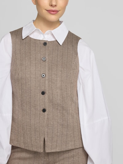 Frauenmodel trägt Weste mit Viskose-Anteil Modell 'Bonnie' von FREE/QUENT in Beige mit Knopfleiste, tailliert, Nahaufnahme Oberkörper. Elastischer Material-Mix, dezentes Fischgrät-Muster, glatte Textur, Kontext: Damen Weste, Schulterbreite 36 cm, Brustweite 48 cm, Rückenlänge 52 cm.