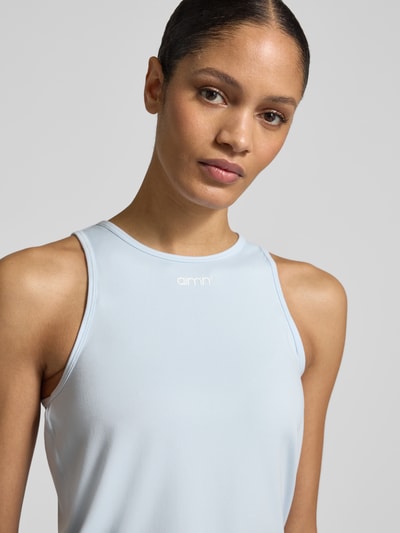Modelka kobieca nosi Top mit Rundhalsausschnitt und Logo od aim'n, materiał z domieszką stretchu, krój regular fit, jasnoniebieski, logo z przodu, długość tyłu 54 cm w rozmiarze S, zbliżenie na górną część ciała, przód