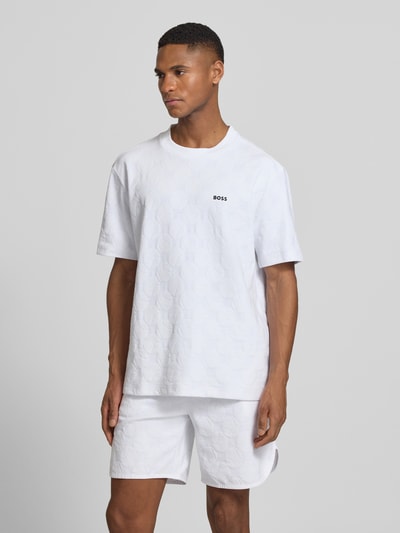 Männermodel trägt Regular Fit T-Shirt aus Baumwoll-Mix Modell 'TS_MEMBER' von BOSS Green in Weiß mit feinem Strukturmuster, Label Print, Ganzkörperansicht von vorne.